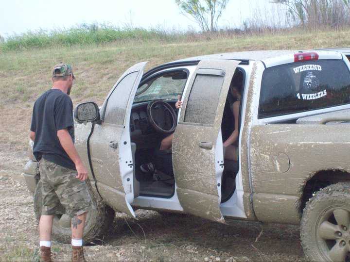 Mud-covered white pickup truck with doors open, showing interior and a person inside