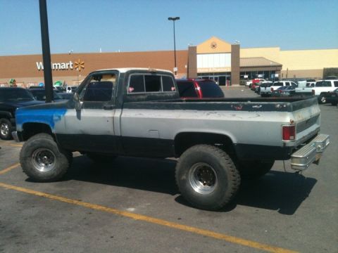 1989 Ford Bronco - A lifted pickup truck with a two-tone paint job is parked in a lot in front of a store.