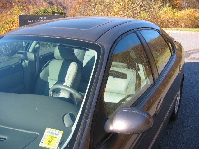Interior of a dark sedan, showing front seats, steering wheel, and sunroof. A parking pass is on the dashboard