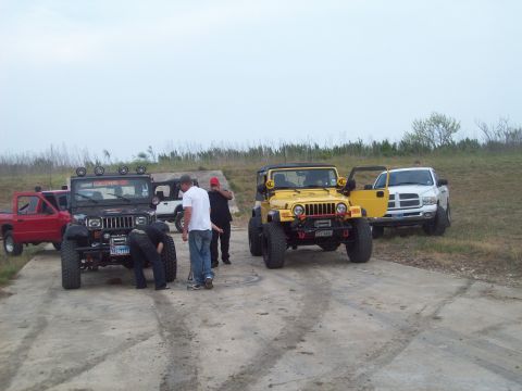 1989 Ford Bronco - Several off-road vehicles are parked together on a dirt surface under an overcast sky.