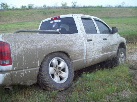 1989 Ford Bronco - Pickup truck covered in mud, stuck in grassy terrain. Features a 'Weekend 4 Wheelers' sticker.