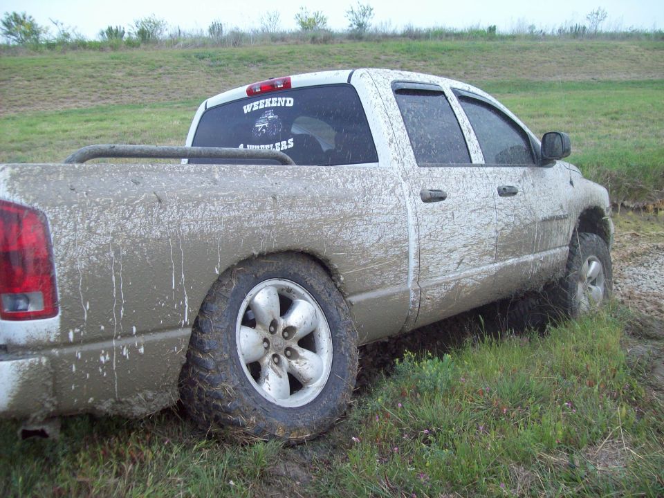 Mud-covered pickup truck stuck in grass with 'WEEKEND 4 WHEELERS' sticker on rear window