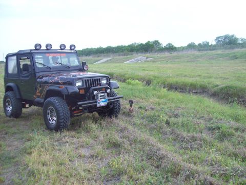 1989 Ford Bronco - This Jeep Wrangler features custom lightning graphics and a roof-mounted light bar, seen off-road in a grassy area.