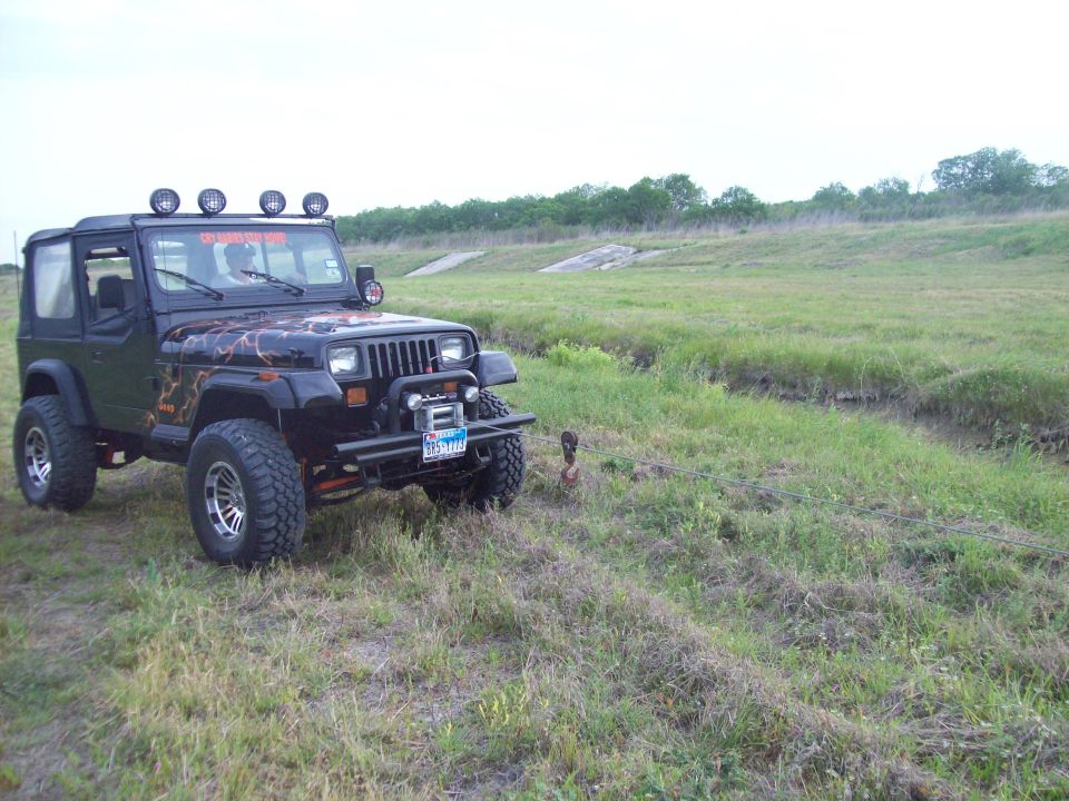 Black Jeep Wrangler with custom graphics and light bar, parked in a grassy field
