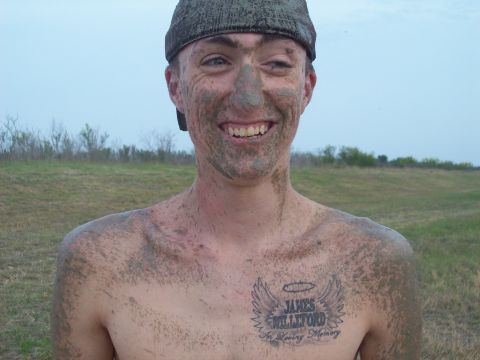 1989 Ford Bronco - A person covered in mud grins widely, with a tattoo visible on their chest.