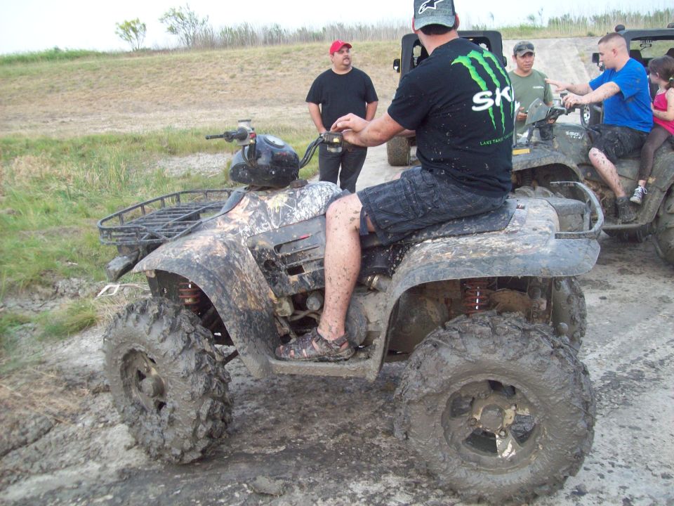 guy on a muddy ATV, another ATV behind him with people on it