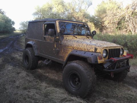 1989 Ford Bronco - A yellow Jeep Wrangler, heavily coated in mud, navigates a muddy trail.