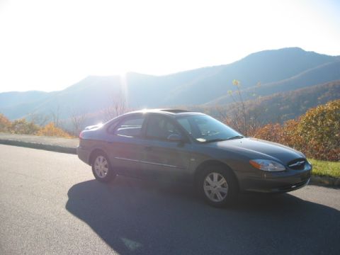 2003 Ford Taurus - A dark 2003 Ford Taurus sedan is parked on a scenic mountain road during a sunny day.