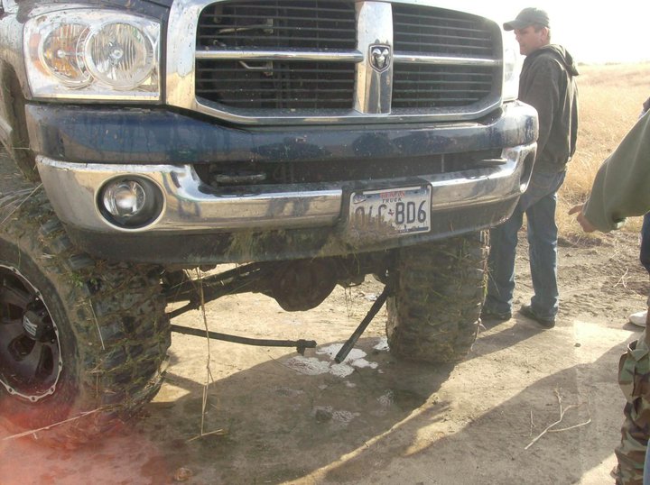 Dark blue pickup truck front end with chrome grille and bumper, lifted suspension, large tires, and a license plate reading OLC-806