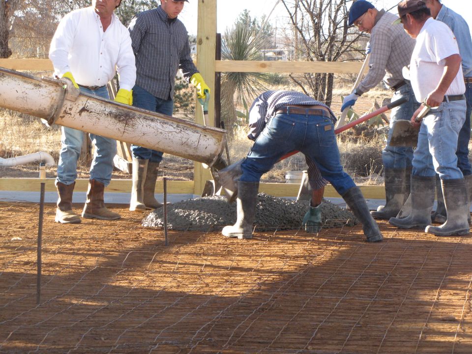 Workers pour concrete from a chute onto a rebar grid
