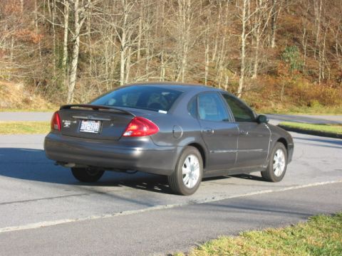 2003 Ford Taurus - A dark gray 2003 Ford Taurus sedan is parked on the side of a road with trees in the background.