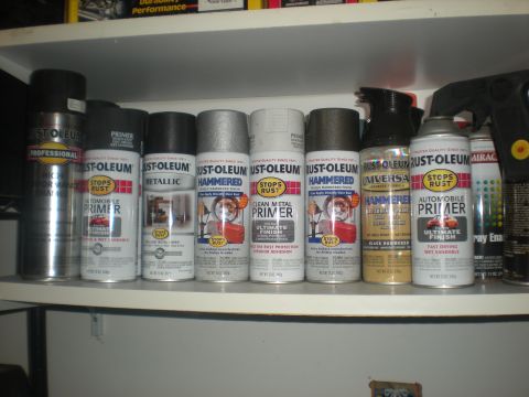 1978 Ford Bronco - A collection of spray paint and primer cans are neatly arranged on a shelf.