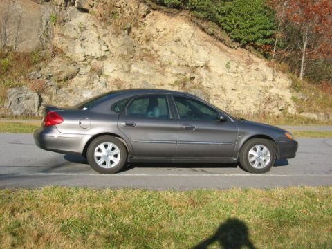 2003 Ford Taurus - A gray 2003 Ford Taurus sedan is parked on the side of a road with a rocky hill in the background.