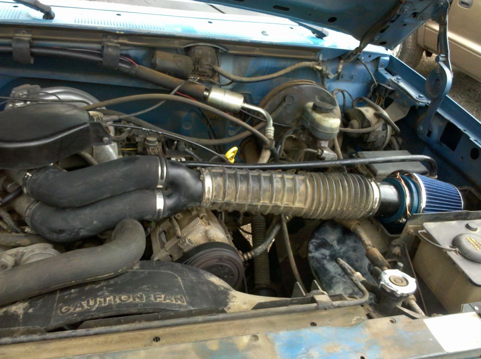 Engine bay with aftermarket air intake and blue filter. Shows hoses, belts, and some engine components