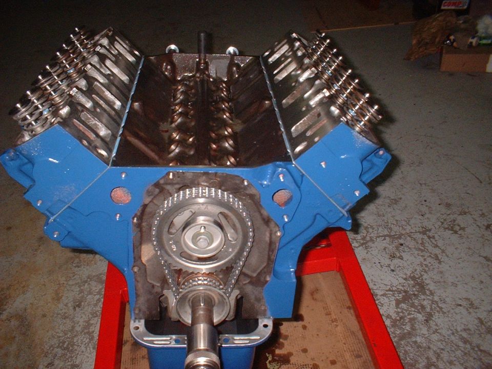 Blue engine block with exposed timing chain and gears, mounted on a red stand
