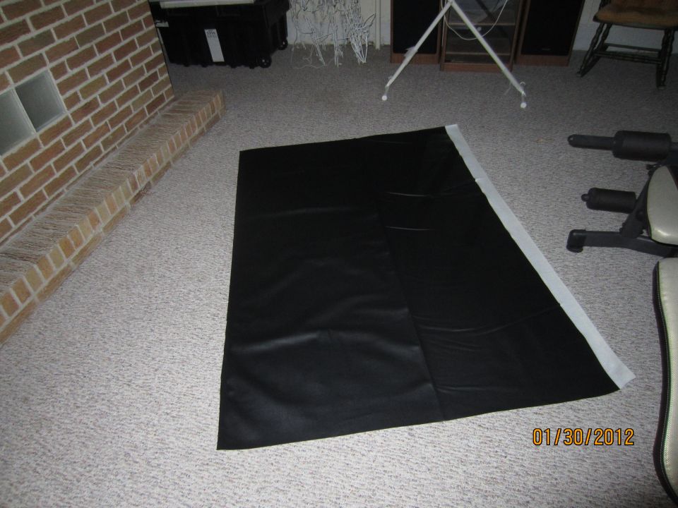 Black vinyl flooring laid out on carpet, with a brick fireplace and weight machine visible