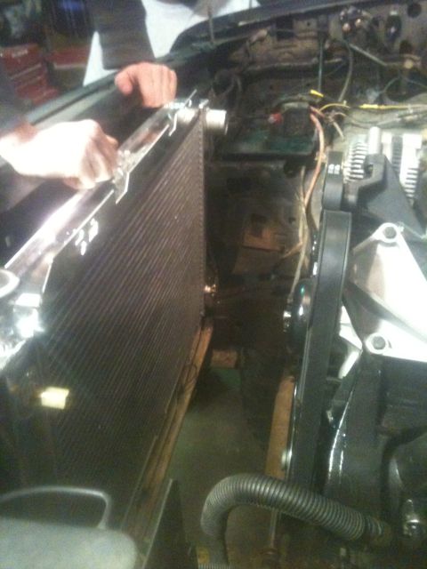 1993 Ford Bronco - Close-up view of engine bay components, including a radiator and belts, with hands visible working on the radiator.