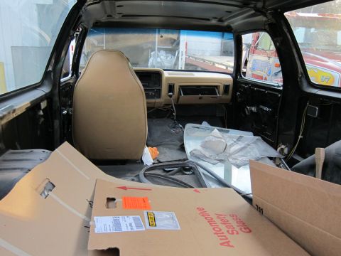 1987 Dodge 1500 - The interior of a 1987 Dodge 1500 pickup truck, viewed from the rear, with tan seats and dashboard visible, along with cardboard boxes in t…