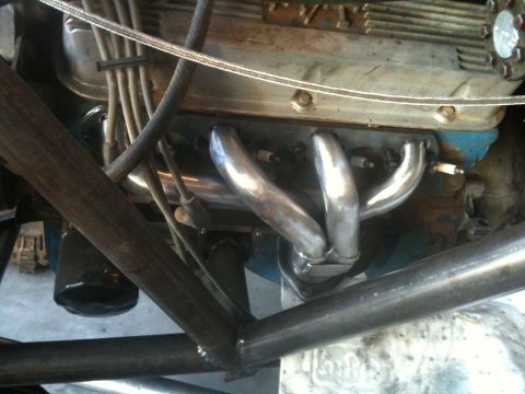 1966 Ford Bronco - Close-up view of an engine's exhaust headers and spark plug wires, with visible roll cage tubing.