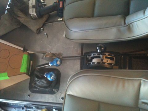 1966 Ford Bronco - Interior view of a vehicle's floor with dual shifters and seats, plus a power tool in the background.