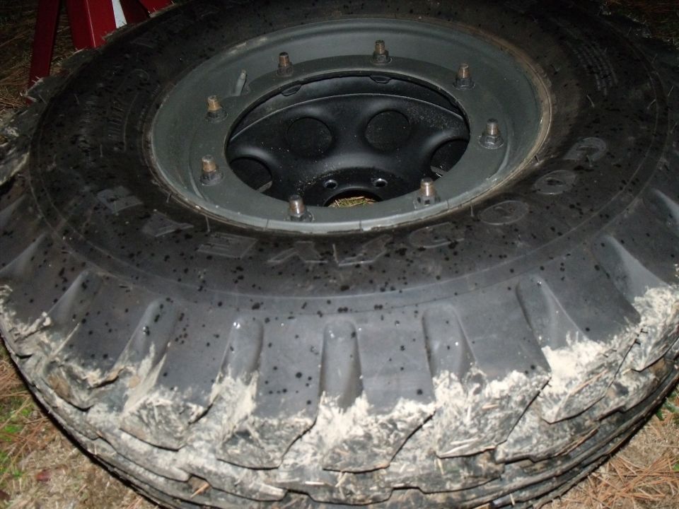 Close-up of a large, muddy off-road tire mounted on a black wheel with several lug nuts visible