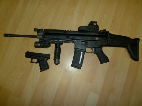 1992 Ford Mustang - An assault rifle with an attached red dot sight and tactical flashlight is displayed alongside a compact handgun on a wooden floor.