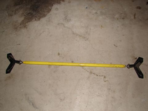 1992 Ford Taurus - A yellow strut bar with black end mounts is shown on a concrete surface.