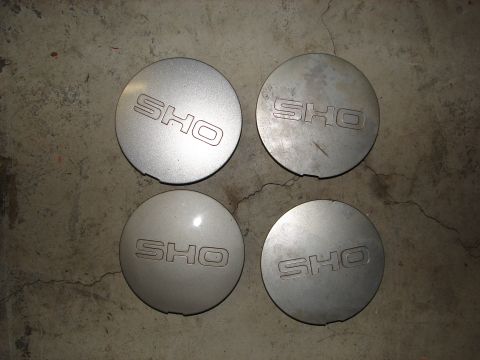 1992 Ford Taurus - A set of four SHO branded hubcaps are displayed on a concrete surface.