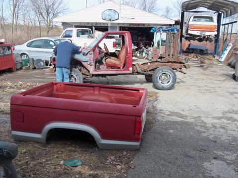 1987 Ford Ranger - A disassembled 1987 Ford Ranger pickup truck sits in a yard, with its chassis and a detached red bed in the foreground.
