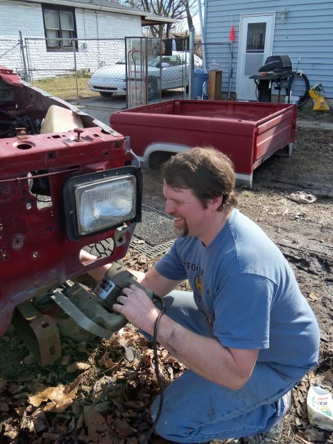 1987 Ford Ranger - Man works on the front end of a red 1987 Ford Ranger, with a truck bed and another vehicle in the background.
