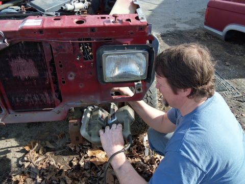 1987 Ford Ranger - A man is working on the front of a red truck, possibly a 1987 Ford Ranger. Another truck is parked behind it.