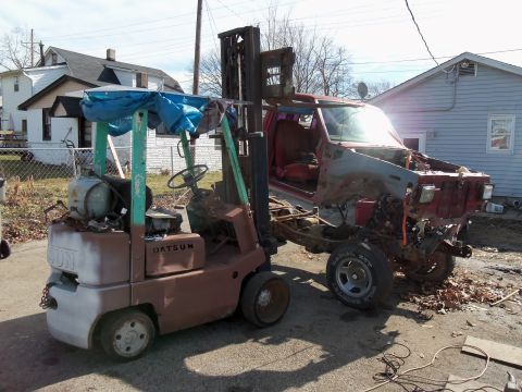 1987 Ford Ranger - A Datsun forklift sits beside a heavily damaged red pickup truck chassis.