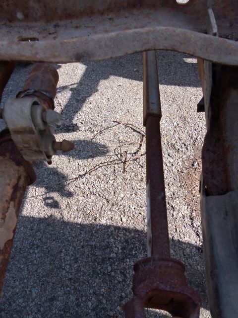 1987 Ford Ranger - Close-up view of heavily rusted vehicle frame components and a driveshaft, resting on a gravel surface.