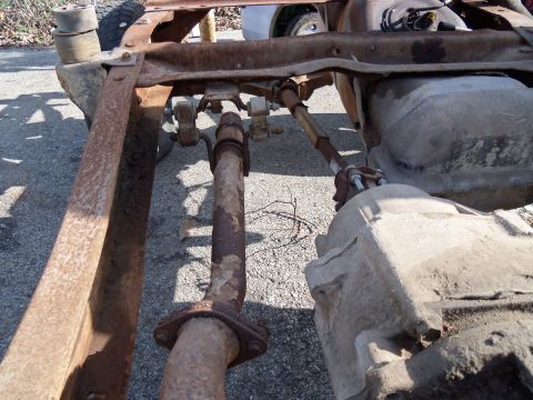 1987 Ford Ranger - Close-up view of the undercarriage of a heavily rusted truck, showing the drivetrain and fuel tank.