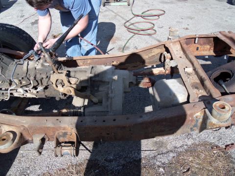 1987 Ford Ranger - A person is working on the transmission and frame of a vehicle that is in a state of disassembly.