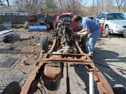 1987 Ford Ranger - A person works on a disassembled truck chassis in a junkyard setting.