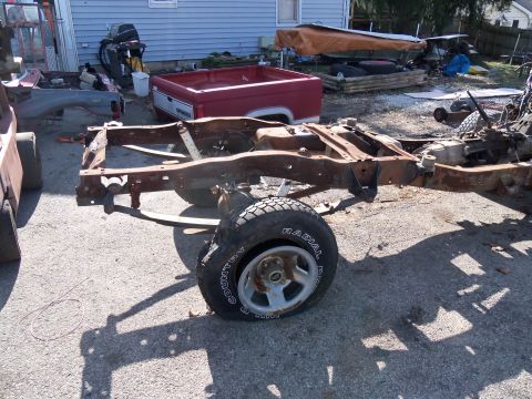 1987 Ford Ranger - Disassembled truck frame and red bed sit in a yard, with a single tire and wheel in the foreground.