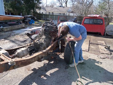 1987 Ford Ranger - Man works on a disassembled truck frame in a yard with other vehicle parts visible.
