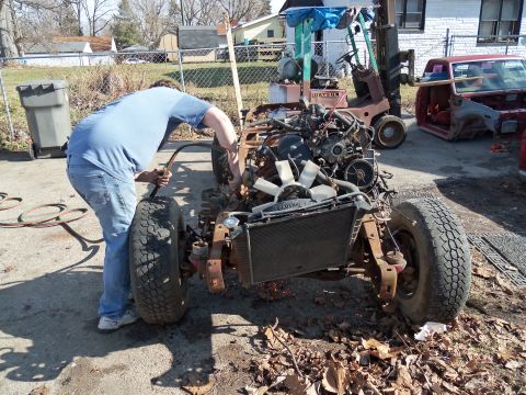 1987 Ford Ranger - A person works on the engine and chassis of a disassembled vehicle outdoors, with another vehicle body visible.