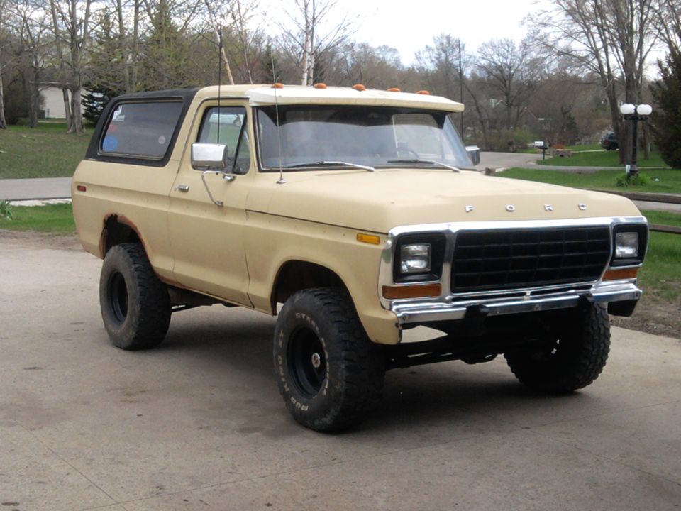 Tan Ford Bronco SUV, front 3/4 view, black top, lifted on mud tires, parked on driveway