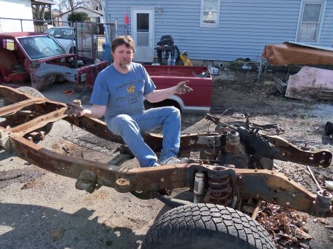 1987 Ford Ranger - A man sits on the frame of a disassembled truck, with other vehicle parts visible in the yard.