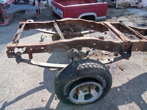 1987 Ford Ranger - Frame and rear axle assembly of a disassembled truck, with another truck bed in the background.