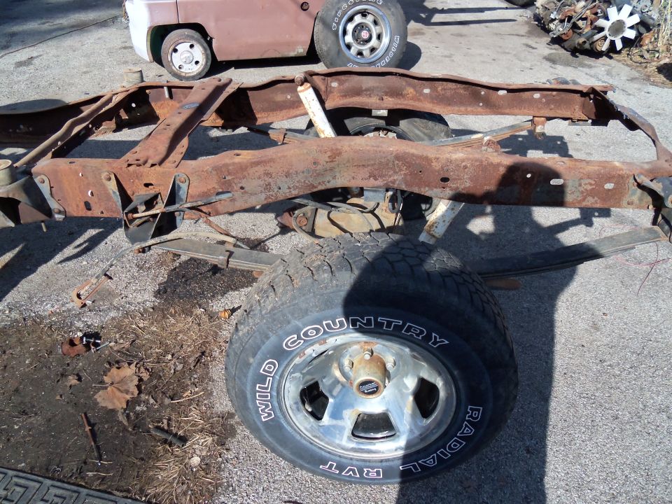 Rusted truck frame with a single tire visible. Text on tire reads 'WILD COUNTRY RADIAL RVT'