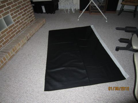 1979 Ford Bronco - A black vinyl sheet is laid out on a carpeted floor, with a brick fireplace and exercise equipment visible in the background.