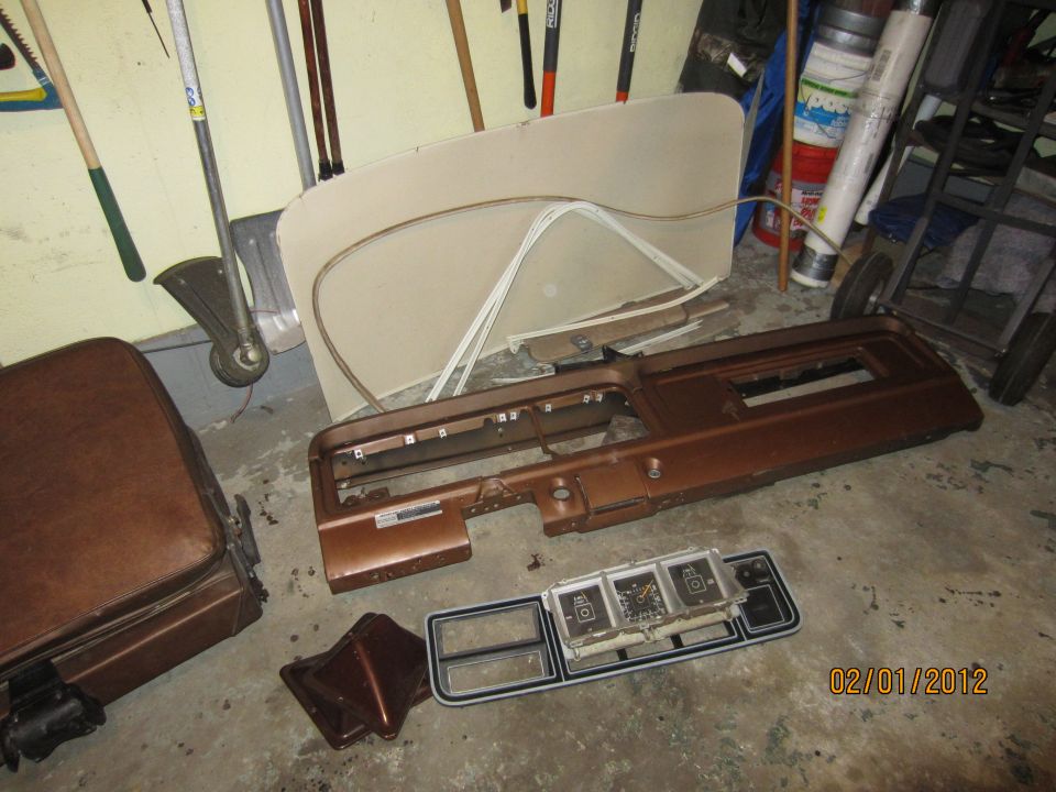 Disassembled brown dashboard and seat parts laid out on a concrete floor, with tools and other items in the background