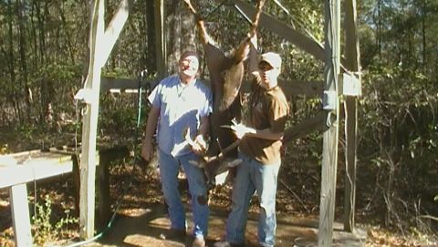 1993 Ford Bronco - Two men pose with a deer carcass hanging from a wooden frame in a wooded area.