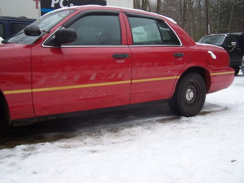 2001 Ford Crown Victoria - Side view of a red sedan with a yellow stripe, parked in the snow. A dark SUV is behind it.