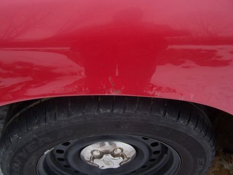 2001 Ford Crown Victoria - A close-up view of a red vehicle's fender and tire, showing a small area of rust.