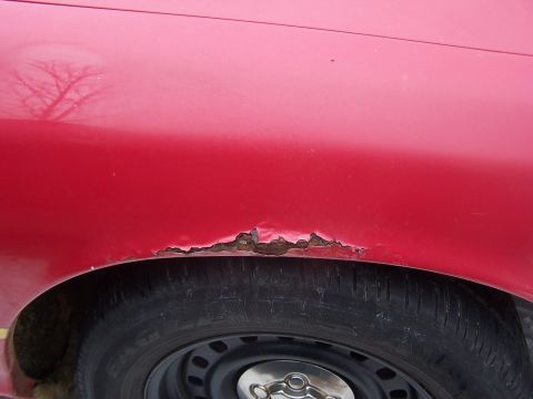 2001 Ford Crown Victoria - Rust damage is visible around the wheel well of a red car.