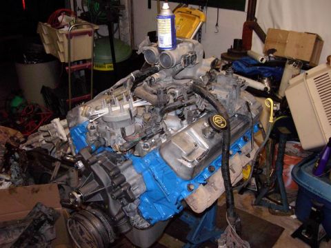1980 Ford Bronco - Engine assembly on a stand, blue painted block and silver valve covers, with various tools and parts in the background.